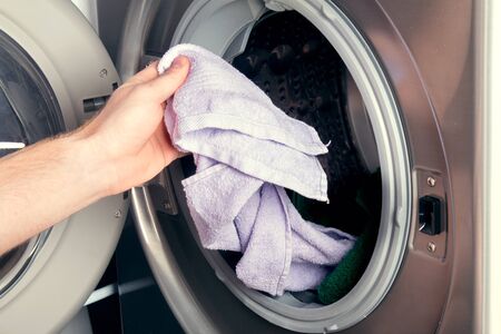 Man taking color clothes from washing machine. A drum of washing machine full of dirty laundry in bathroom.の写真素材