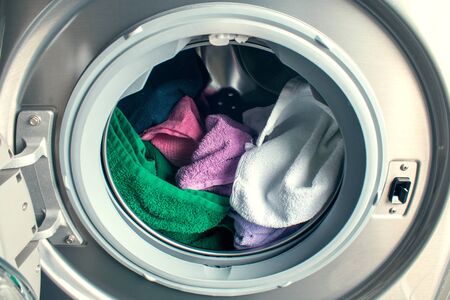 Man taking color clothes from washing machine. A drum of washing machine full of dirty laundry in bathroom.の写真素材