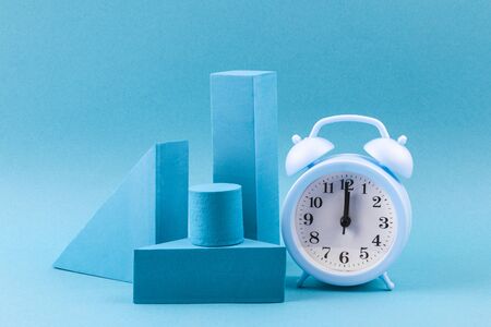 Blue geometric shapes with an alarm clock on a blue background. Template composition for...