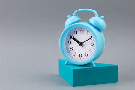 Alarm clock on grey background - time concept. An alarm clock on a geometric figure.