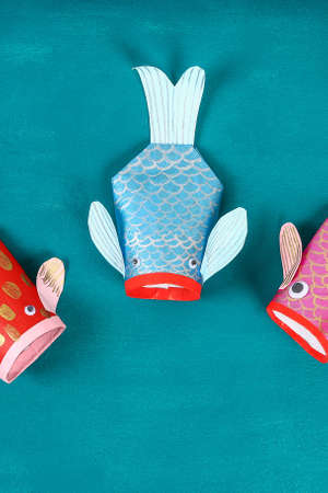 Diy koi carp fish on blue green background. Gift ideas, decor for the Chinese new year. Kid handmade. Carp koi fish of paper, toilet roll, googly eyes. Step by step. Process children crafts. Top view.の写真素材