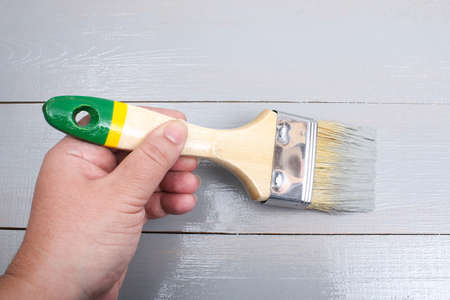 Brush with can paint in hand. A man paints wooden boards in a gray paint brush.