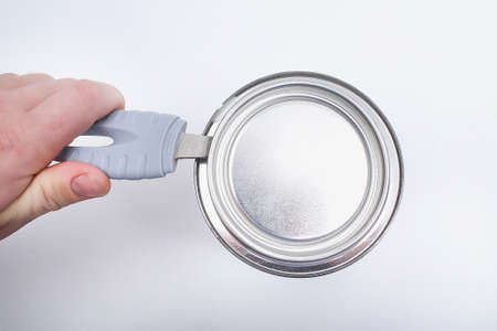 A man opens a jar of white paint with a can opener on a white background. Renovation concept.の写真素材