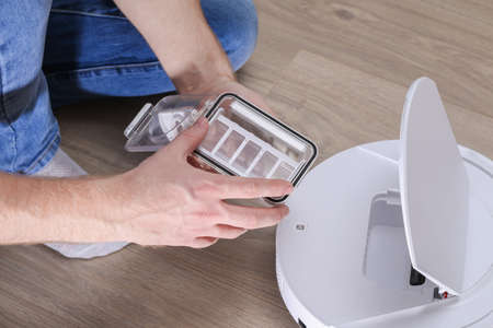 A man inserts a filter and a container to collect dust and debris into a robot vacuum cleaner.の写真素材