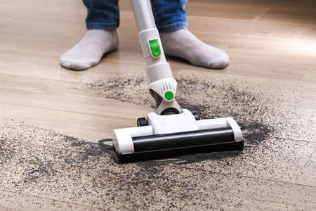 A man uses a bagless vertical cordless vacuum cleaner to clean the floor.の写真素材