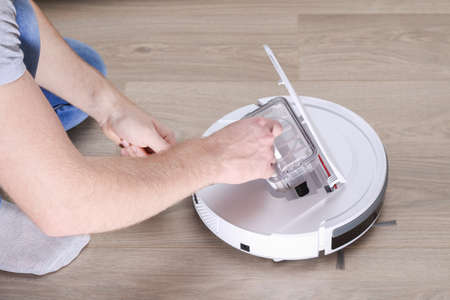 A man inserts a filter and a container to collect dust and debris into a robot vacuum cleaner.