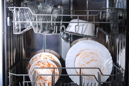 A man loads dirty dishes, plates, spoons, forks, cutlery into the dishwasher tray.の写真素材
