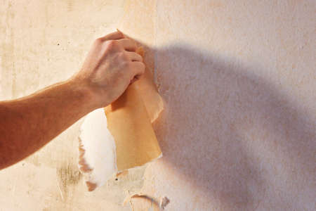 A man removes old wallpaper with a spatula and a spray bottle with water.の写真素材