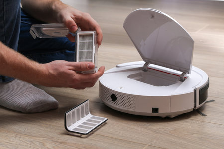 A man inserts a filter and a container to collect dust and debris into a robot vacuum cleaner.の写真素材