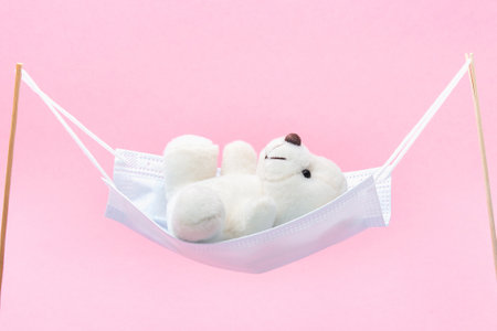 The white teddy bear is swinging in a medical mask like in a hammock or swing.の写真素材