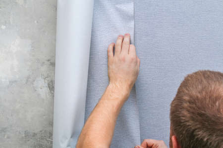 A man glues gray vinyl wallpaper on a non-woven backing. Renovation of the room.の写真素材