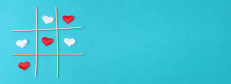 Playing tic tac toe with a white heart and a red heart on a blue background. Concept for love day,...