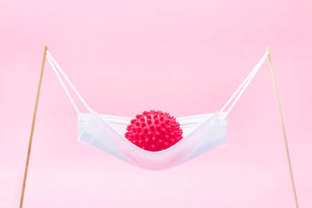 A red ball with spikes coronavirus swinging in a medical mask like in a hammock or swing.