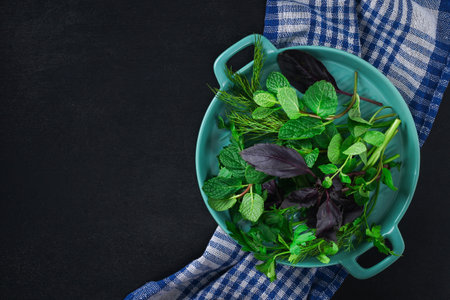 Green culinary herb on a black background. Parsley, dill, mint, basil in a blue dish. Top view.