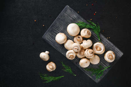 Raw mushrooms champignons on a wooden board on a black background. Top view. Cooking champignons.の写真素材