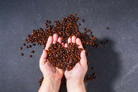 Roasted brown coffee beans on a gray background. Template for advertising coffee in shape heart in hand. Top view.の写真素材