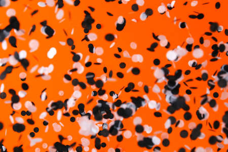 White black confetti flying on orange background. Halloween party.の写真素材