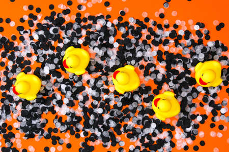 Yellow ducks swim among white black confetti. Halloween decorations orange background. Halloween concept. Flat lay, top view.の写真素材