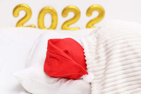 A man sleeps in a Christmas hat against the background Number 2022 written with balloons. New Year...