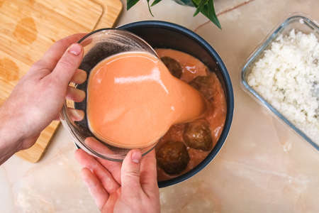A man puts lazy cabbage rolls into a multicooker bowl and pours tomato and sour cream sauce over...
