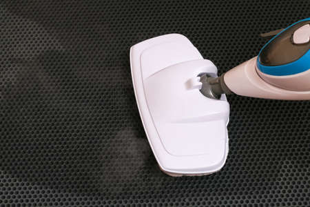 A man washes a black honeycomb door mat with a steam mop. Killing germs, clean floor, decontamination.の写真素材