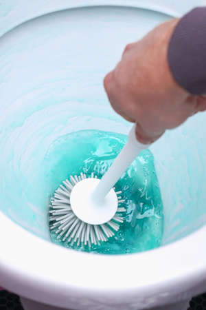 A man washes the toilet with a silicone brush and cleaner. Cleaning of the house, bathroom.