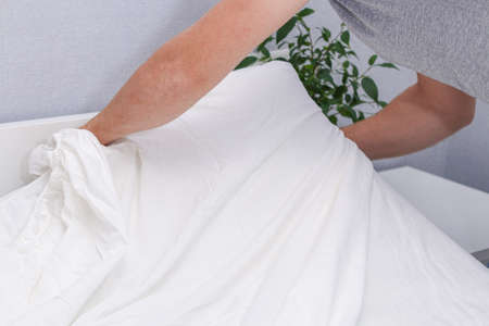 A man puts an elasticated sheet on the mattress. Change of bed linen.