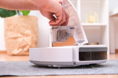 A man takes out a garbage container from a robot vacuum cleaner. The container is full of wool, dust, hair.の写真素材