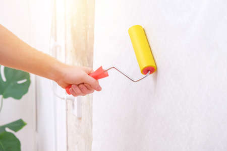 A man rolls out a canvas of white wallpaper with a suture wallpaper yellow roller. Removing air bubbles and glue from under the wallpaper. Wallpapering. Repair of a room, apartment, house.の写真素材