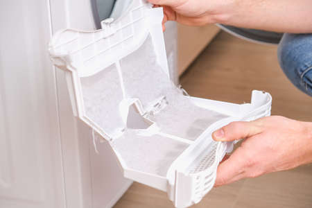 A man takes a lint filter out of the dryer and cleans it from dust, lint, hair, wool.の写真素材