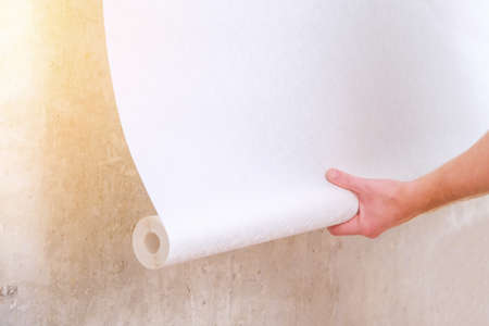 A man rolls out a roll of white wallpaper on the wall with glue. Wallpapering. Repair of a room, apartment, house.の写真素材