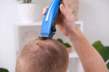 A man cuts his hair with a clipper. Cutting a short hairstyle at home. Close-up.の写真素材