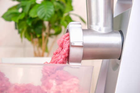 A man processes meat in an electric meat grinder. Preparation of minced beef and pork for cutlets,...