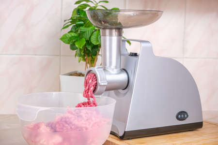 A man processes meat in an electric meat grinder. Preparation of minced beef and pork for cutlets,...