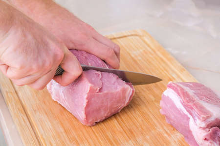 A man cuts meat with a knife on a wooden board. Preparation of minced beef and pork for cutlets, meatballs, chops.の写真素材
