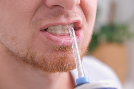 A handsome man cleans his mouth and teeth with a white electric irrigator in the morning close-up.の写真素材