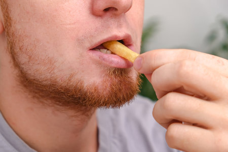 The man bites and chews French fries. A man eats fast food. Unhealthy diet, bad habits.の写真素材