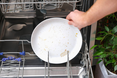 A man loads a dishwasher with dirty dishes. A dirty white saucer. Preparing the dishwasher for...
