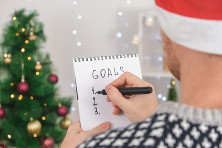 Man writes marker board at white table with Christmas decor goals and plans new year and Christmas....