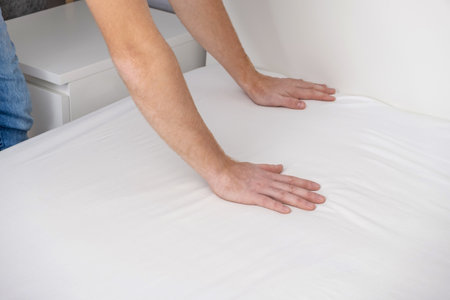 A man makes his cozy bed with fresh bright white bed linen. Making the bed with fresh bed linen by a white man. The day of the change of bedclothes. The day of washing bedclothes in the laundry room.の写真素材