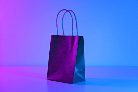 Paper black bag in neon light. The concept of sales, Black Friday, cyber Monday on a blue pink background. Minimalism. Gifts, shopping, shopping.の写真素材