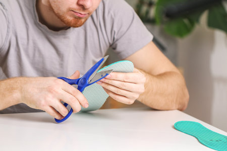 A man cuts out new shoe insoles with scissors to fit his foot size.の写真素材