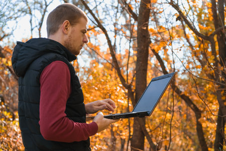 A freelance man works remotely in nature in the autumn forest. Country life. A break from...