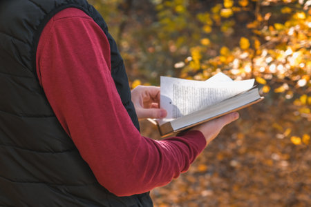 Young man in an autumn park or forest and reading book. Mental recreation in nature. Quiet country...