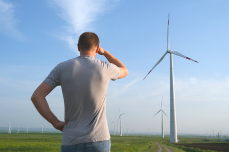 The man stands with his back and looks at the wind turbine. Wind Energy Park.の写真素材