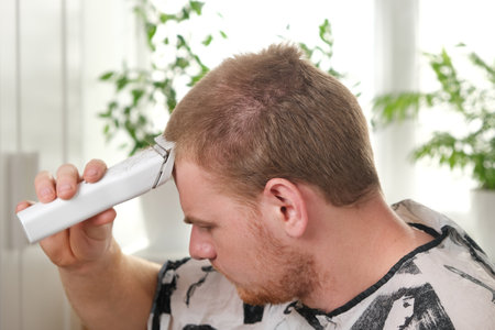 A man cuts his hair with a clipper. Haircut at home. Saving money. Barber shop at home. Change...