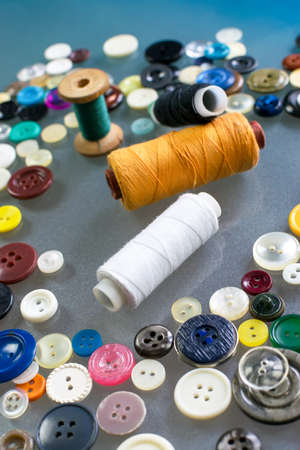 Spools of colored thread lie in the middle of the table surrounded by colorful old plastic buttons....