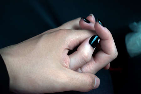 A female hand with a black manicure with a heart pattern is clenched in a male hand. Couple in love...