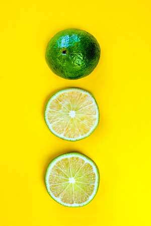 Three fresh sliced lime wedges lie vertically in a row on a bright yellow background