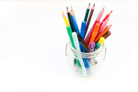 Artist's set. Colored pencils and felt-tip pens lie in purple a jar on a white background